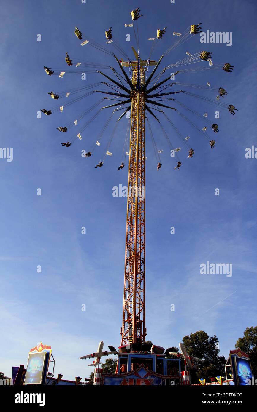 Sehr hohes Kettenkarussell auf gelber Säule mit vielen Passagieren in luftiger Höhe, Oktoberfest München, Bayern, Deutschland Stockfoto