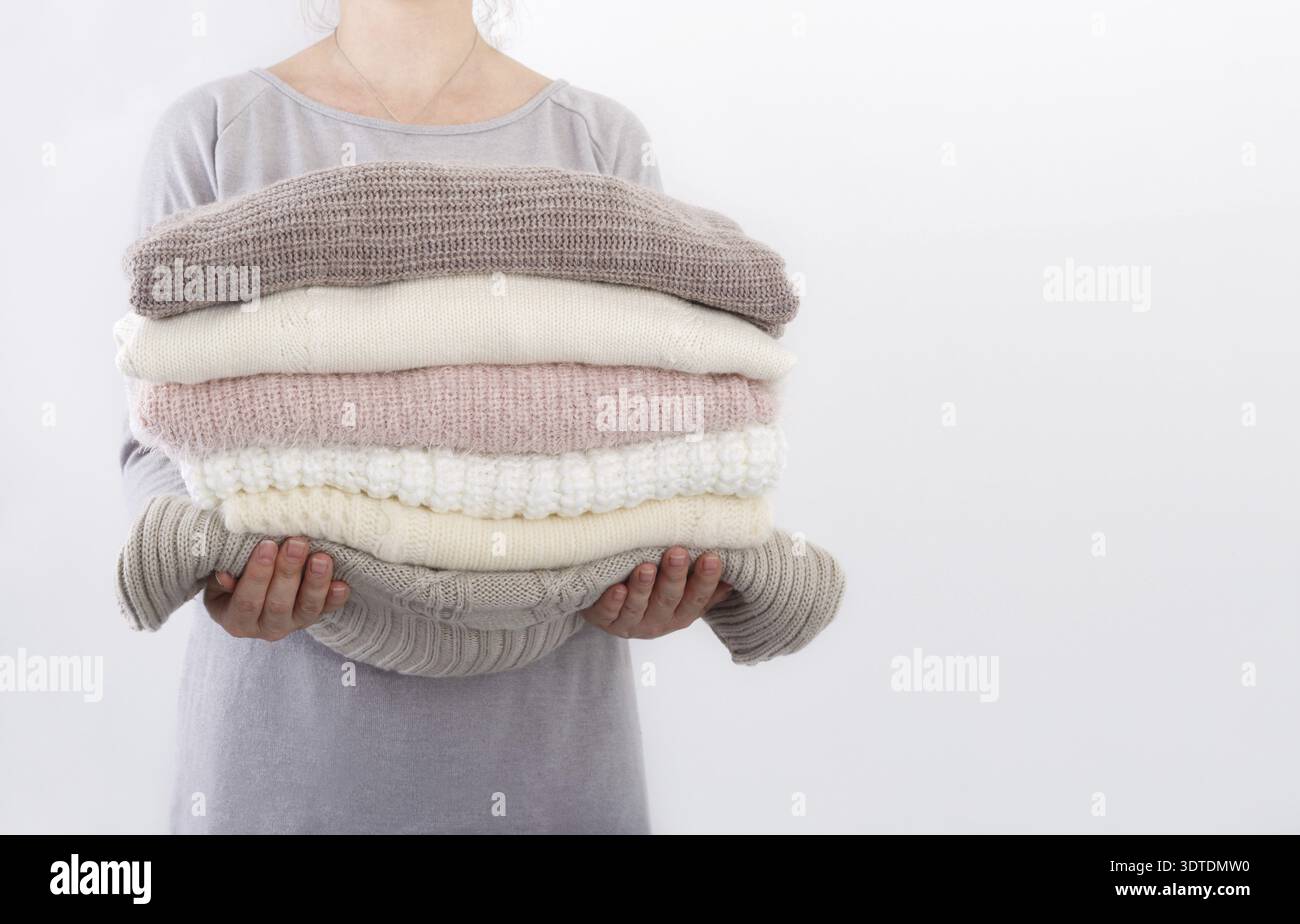 Stapel von gemütlichen gestrickte Pullover oder Decken Pastell Trend Farben in die Hände einer jungen Frau gegen die Wand Stockfoto