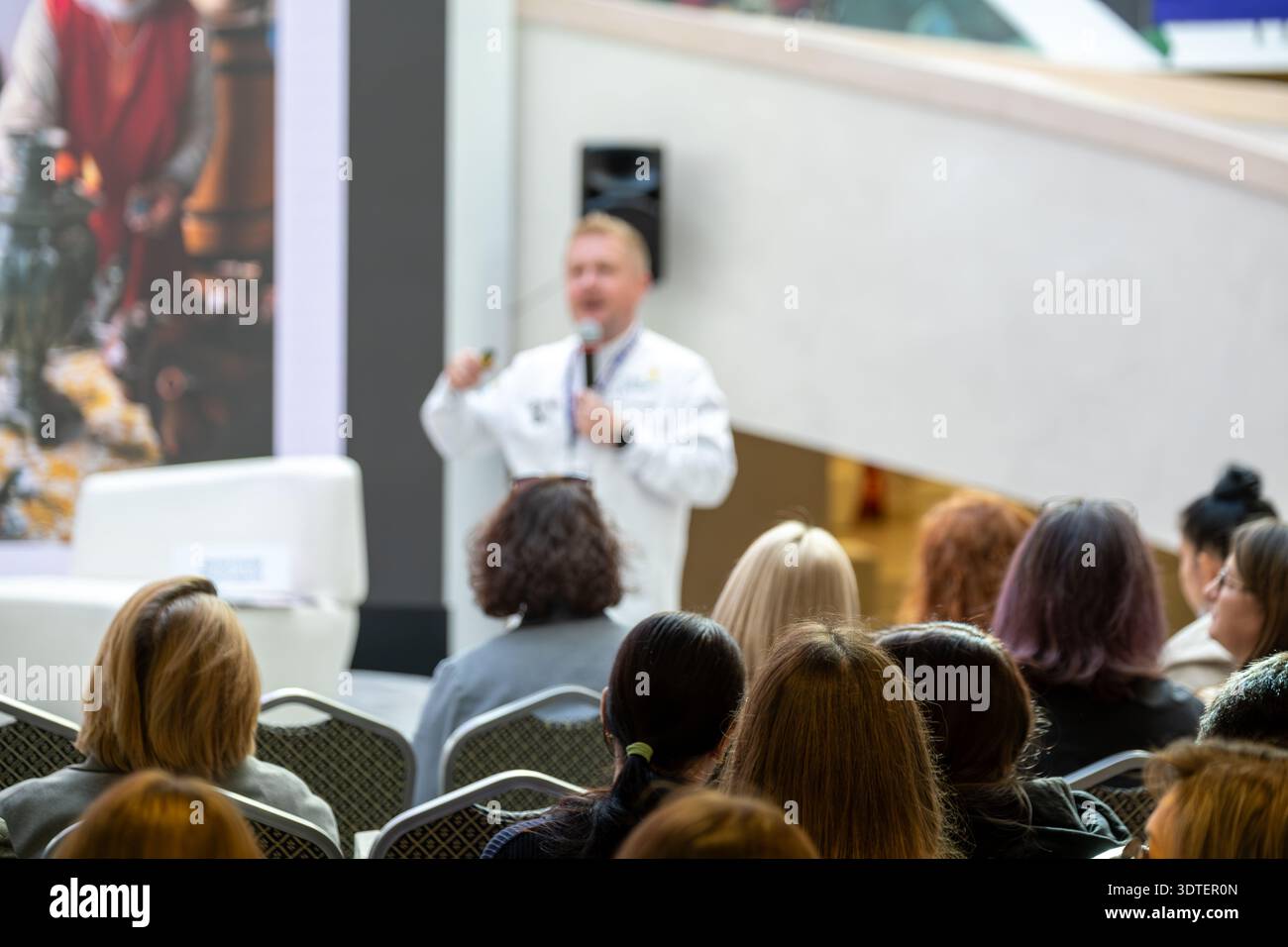 Der Lautsprecher sorgt für Gespräche mit aufmerksamen Gästen in modernen Räumlichkeiten. Das Publikum sitzt in Reihen und sieht die Präsentation. Klare Lichter schaffen eine professionelle Atmosphäre. Die Veranstaltung konzentriert sich auf das Lernen und den Austausch von Ideen. Stockfoto