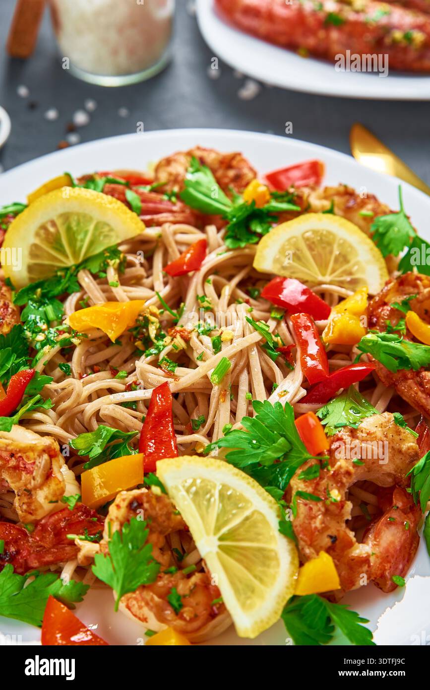 Nudeln mit Garnelen, Zitrone und frischer Petersilie auf weißem Teller unter Rühren braten, Soba mit Garnelen, asiatische Küche, Draufsicht Stockfoto