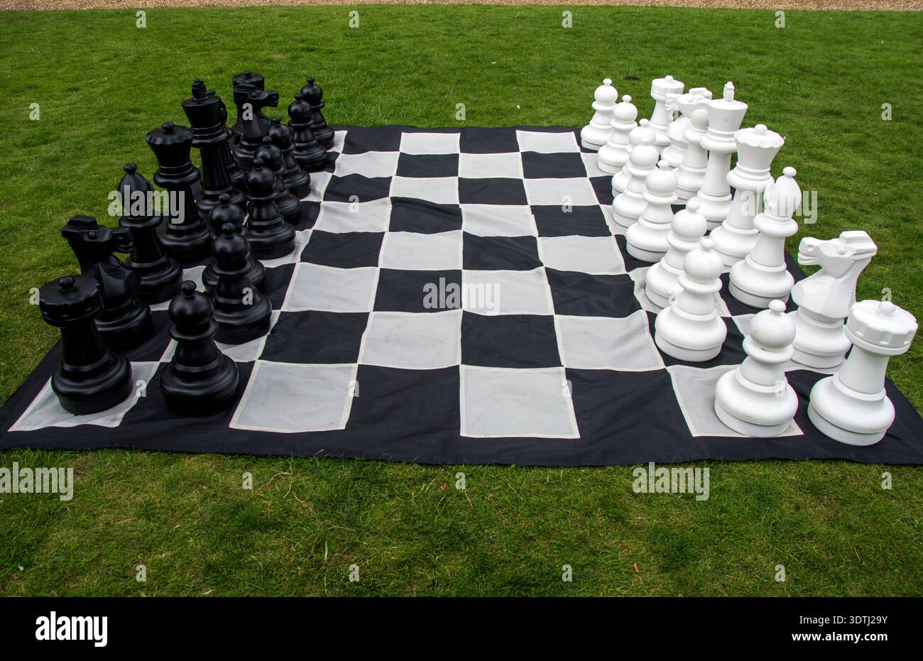 Übergroßes Western Schach-Set im Freien auf einer großen schwarz-weißen karierten Matte auf dem Gras Stockfoto