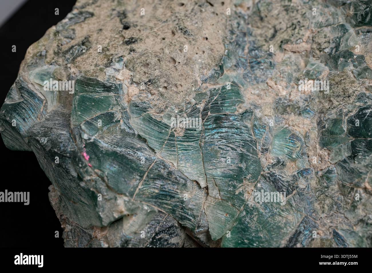 Nahaufnahme eines rauen grünen Mineralgesteins mit mehrschichtigen, faserigen Texturen und beigefarbener Matrix, die Spaltlinien und verwitterte Oberflächen zeigt. Stockfoto