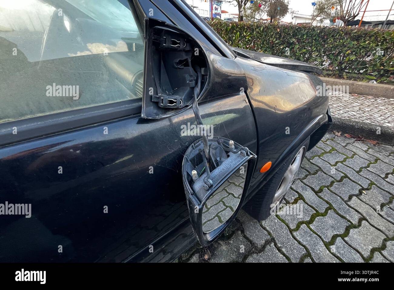 Defekter Seitenspiegel, der an der schwarzen Fahrzeugtür hängt, mit freiliegenden Drähten nach Unfallschäden im Außenbereich Stockfoto