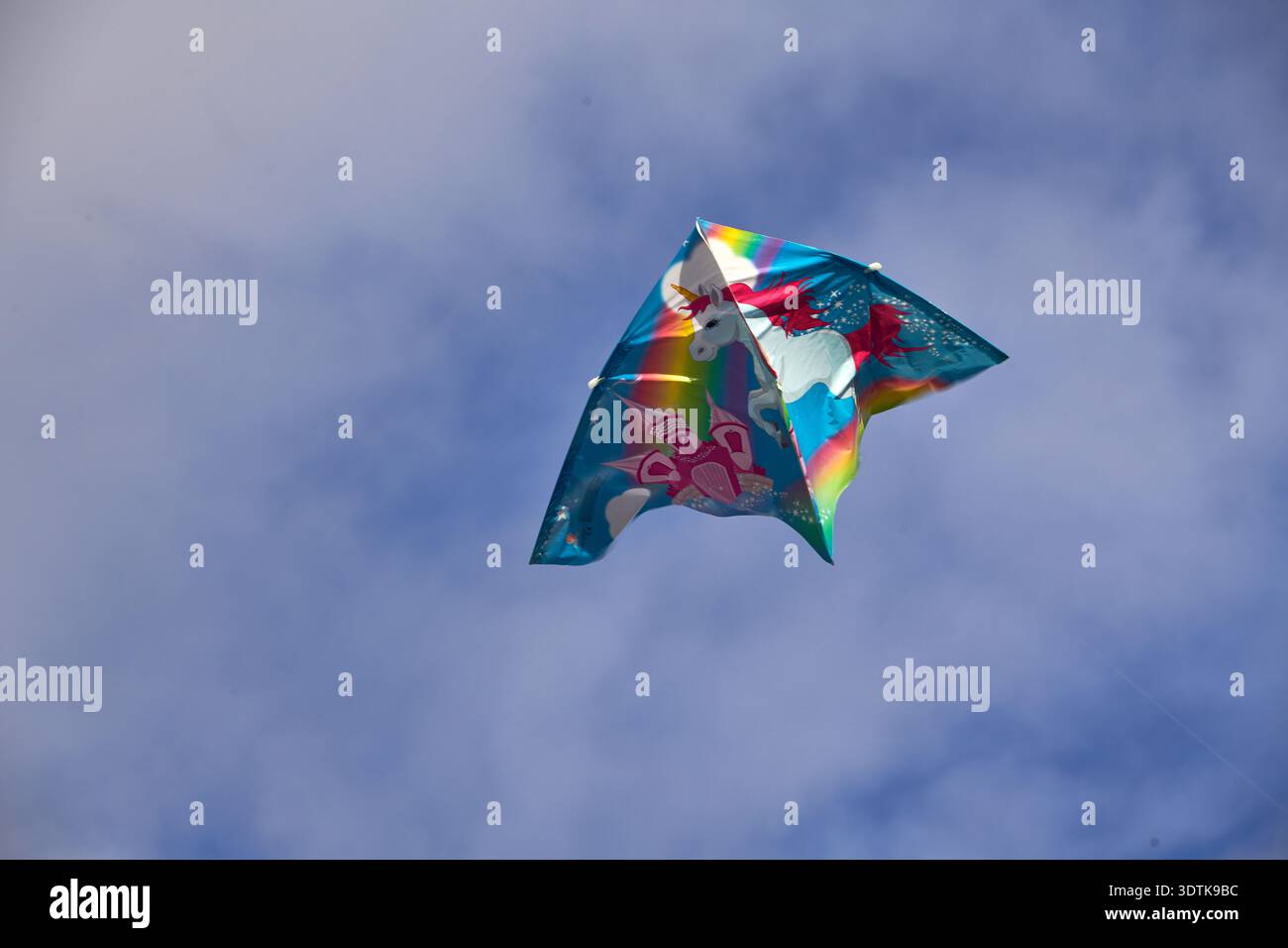 Ein lebendiger, mehrfarbiger Drachen mit einem weißen Einhorn mit Regenbogenmähne und -Schwanz, neben einem rosafarbenen Schloss, das mit so einem klaren blauen Himmel aufsteigt Stockfoto