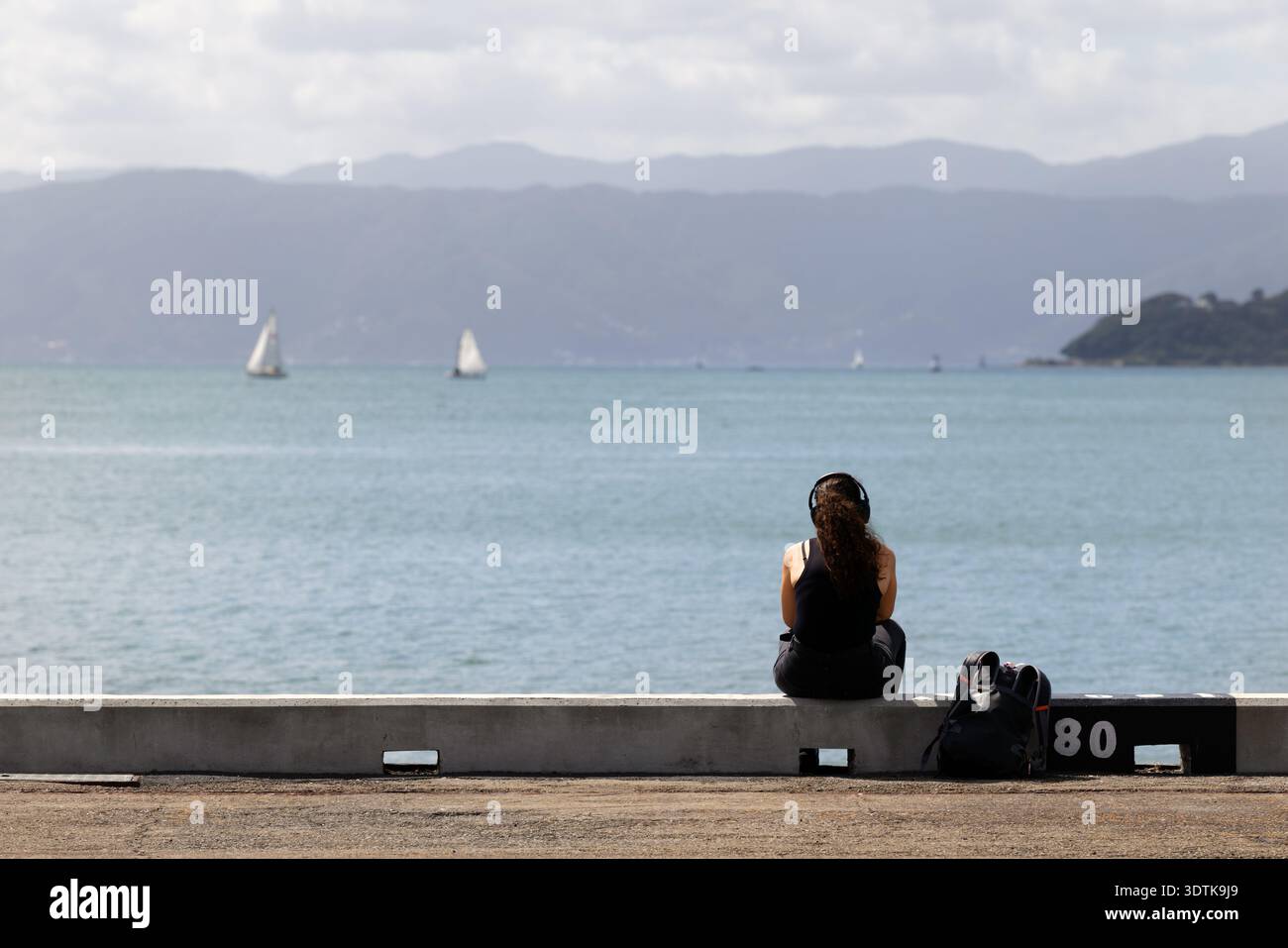 Frau, die am Ufer von Wellington sitzt und den Hafen überblickt, Neuseeland. Stockfoto