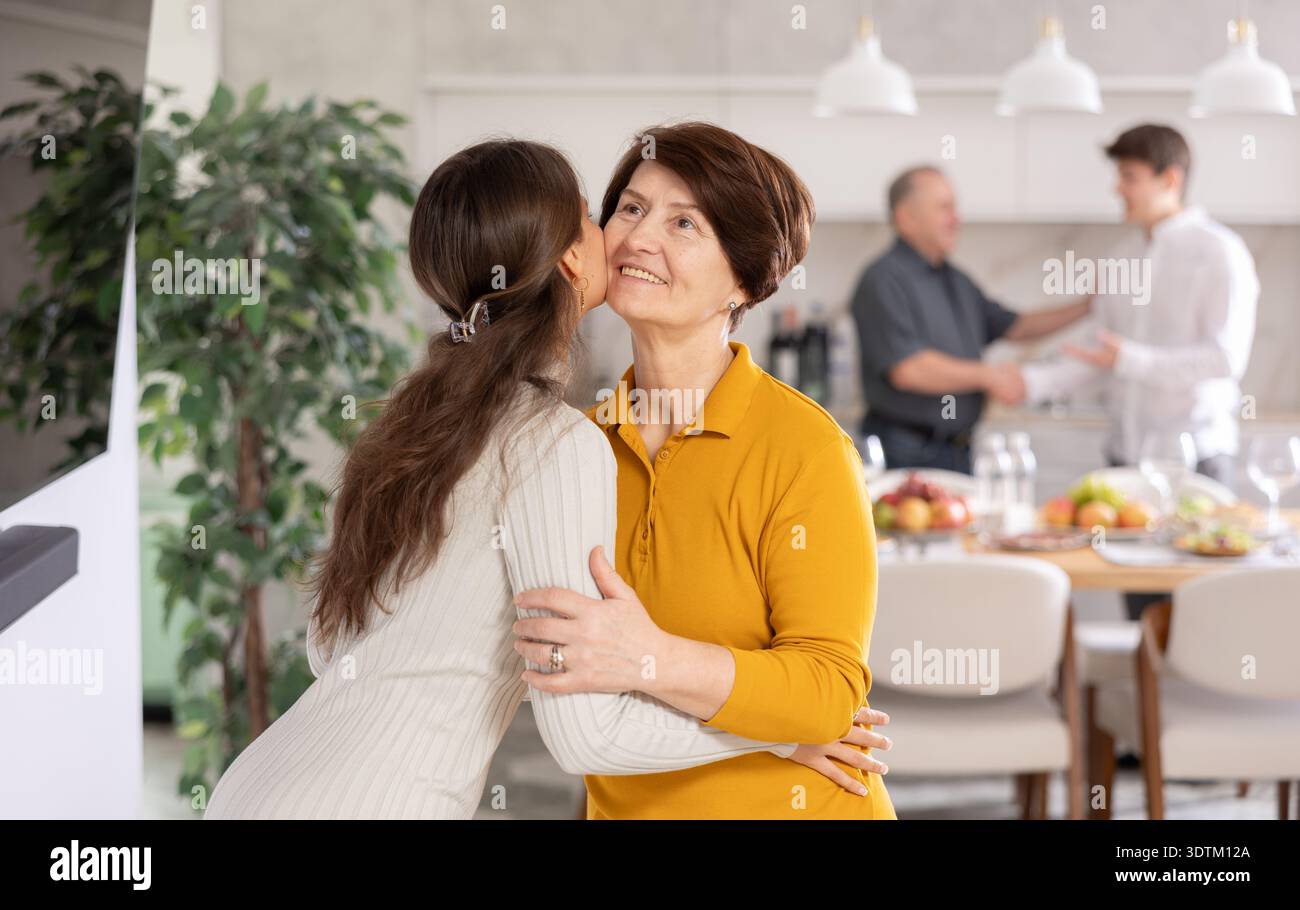 Glückliche Mutter trifft ihre Tochter, umarmt und küsst sie. Im Hintergrund schüttelt Vater Guy Hand Stockfoto