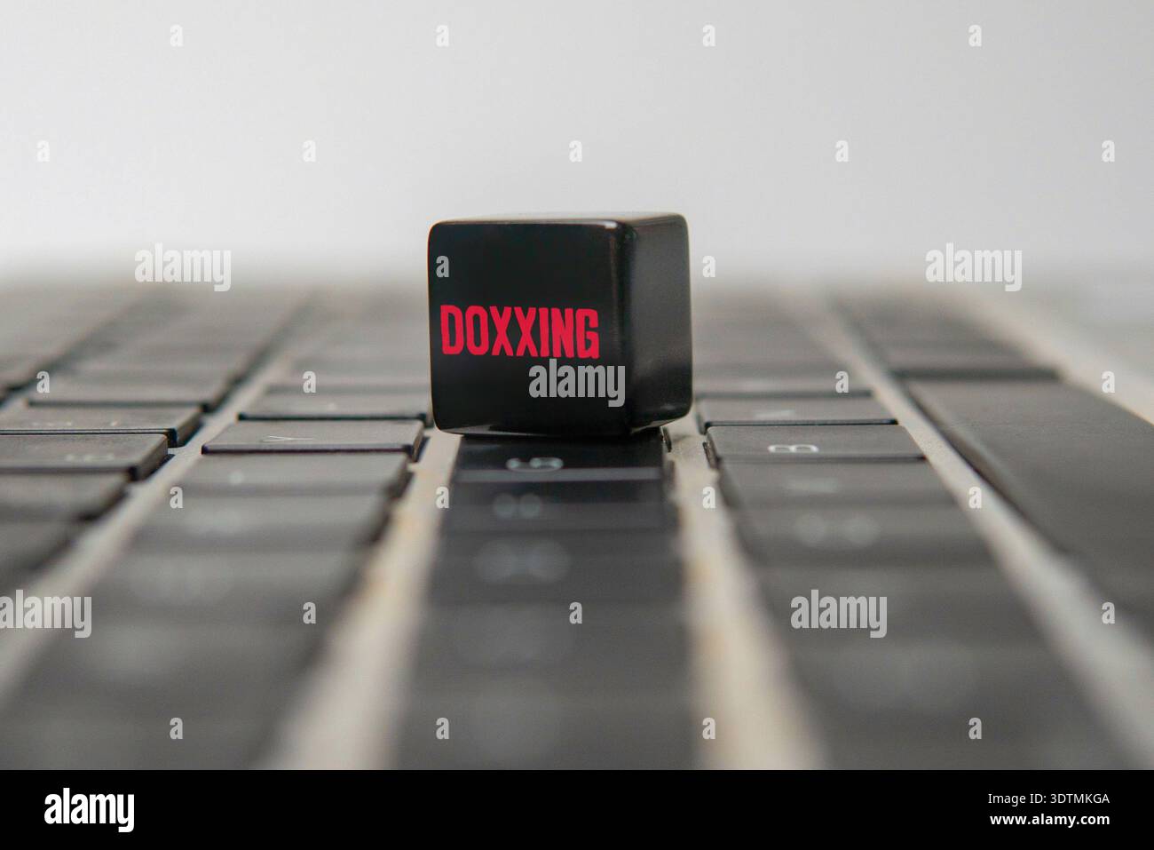 Schwarzer Würfel mit rotem DOXXING-Text auf einer schwarzen Laptop-Tastatur. Cybermobbing, Identitätsdiebstahl, Online-Belästigung und Datenschutzrisiken. Stockfoto