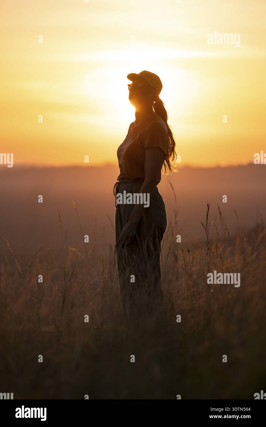 Junge Frau, die bei Sonnenuntergang im hohen Gras steht, Lake Victoria, Uganda Stockfoto