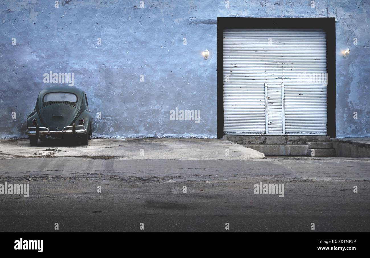 Merida, Yucatan, Mexiko - 26. Januar 2019: Dunkelgrüner Oldtimer Volkswagen Beetle Parkplatz an verlassenen Gebäude mit Garagentor Stockfoto