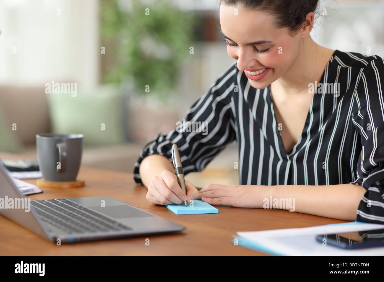 Glücklicher freiberuflicher Mitarbeiter, der mit Stift in blauer Sticky Note schreibt, der zu Hause arbeitet Stockfoto