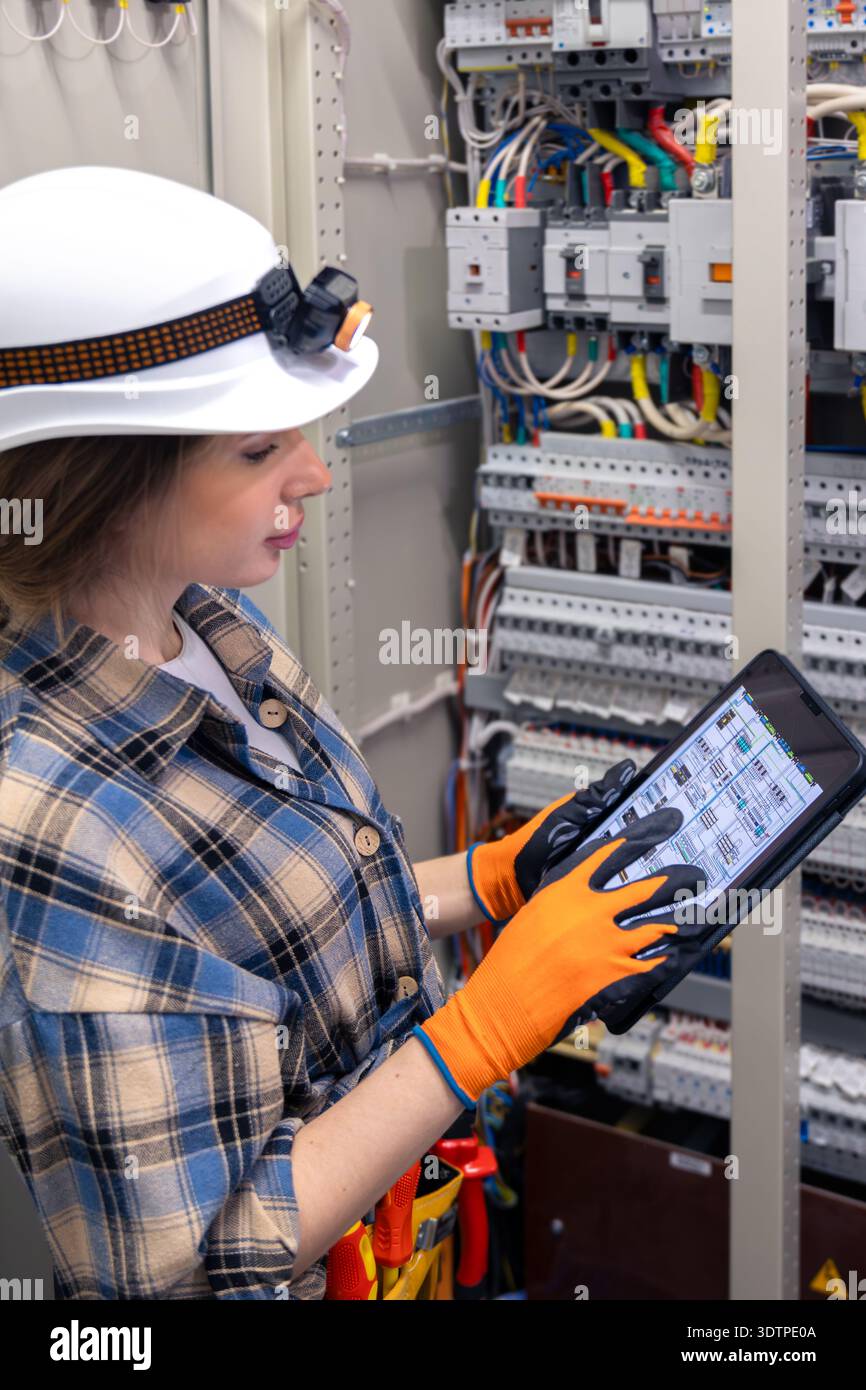 Die Ingenieurin benutzt ein Tablet neben der offenen Zentrale. Schaltplanbildschirm. Stockfoto