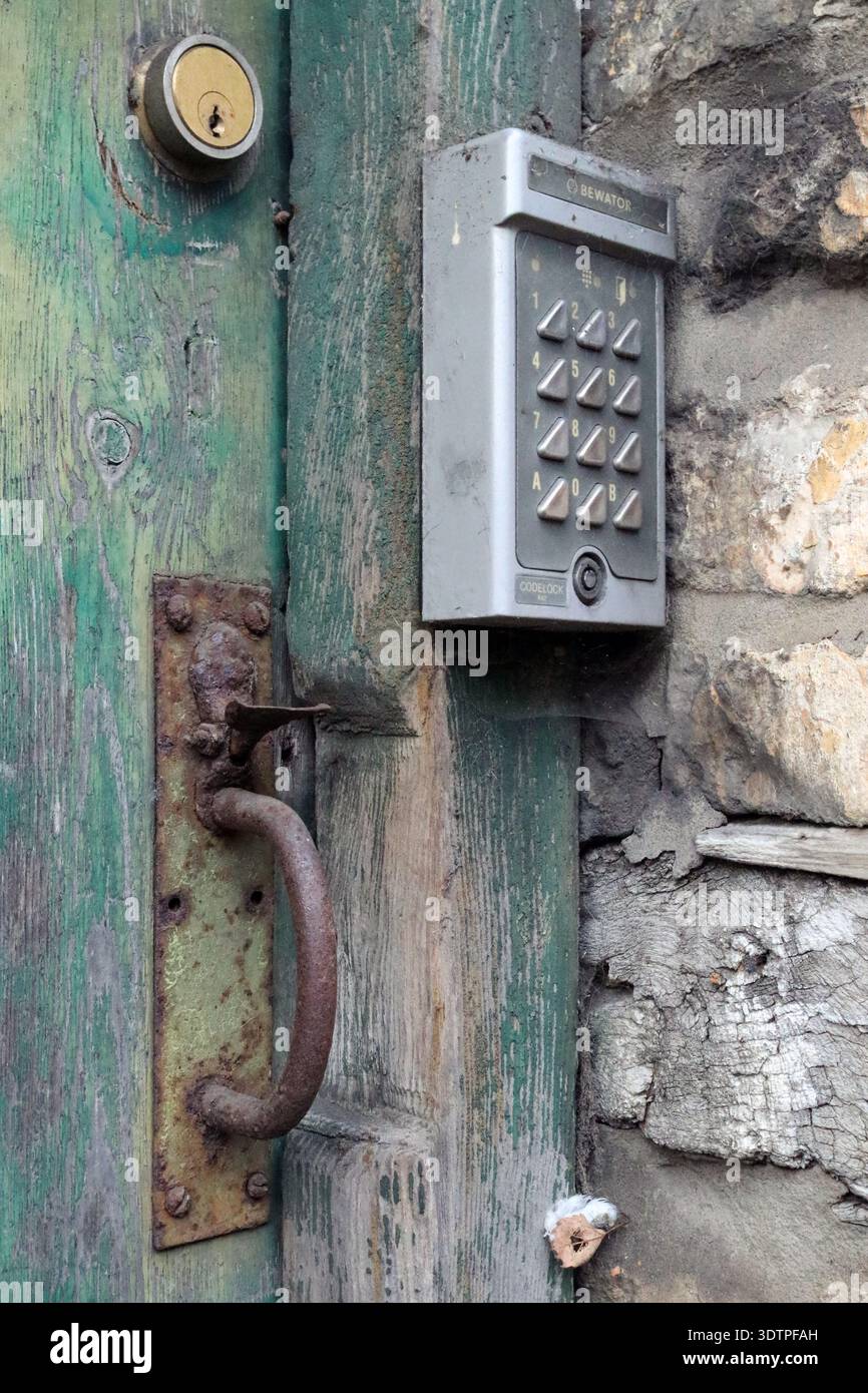 Verwitterte grüne Holztür an der Oxford Street, Malmesbury, Wiltshire, Großbritannien, mit einem rostigen Griff und einem modernen digitalen Bewator-Eingabesystem. Stockfoto