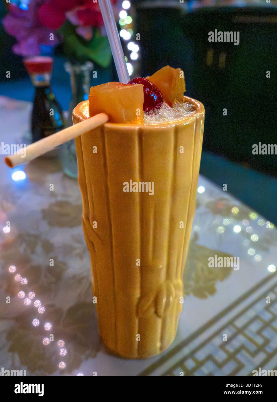 Genießen Sie eine tropische Oase mit diesem lebhaften Mai Tai, serviert in einem charakteristischen Keramikbecher im Bambus-Stil. Garniert mit frischer Ananas und einer Kirsche, ist es nicht Stockfoto