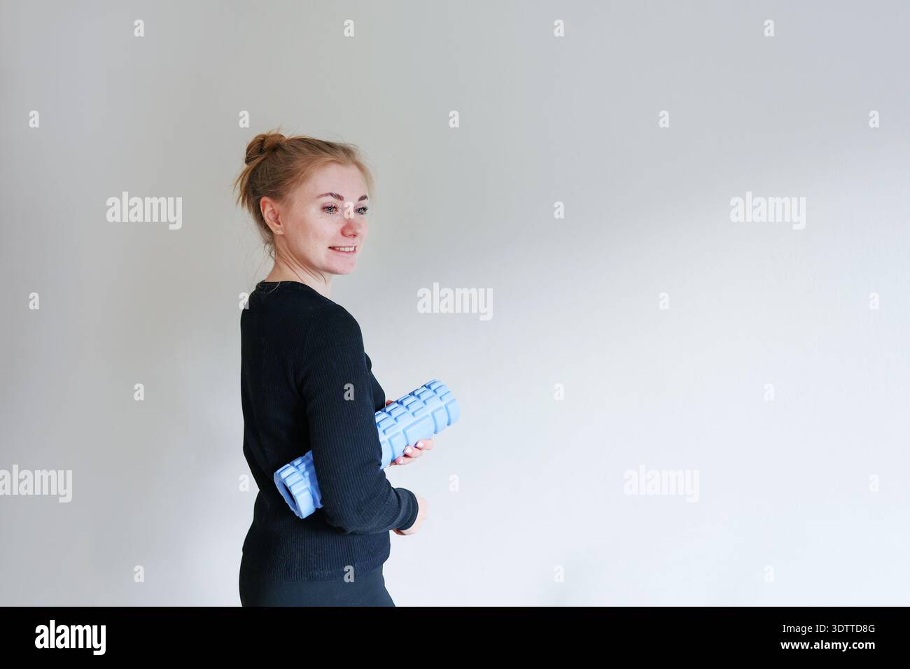 Weibliche Athletin mit Massageroller posiert auf hellem Hintergrund. Physiotherapie, Stretching und gesundes Lifestyle Thema. Stockfoto