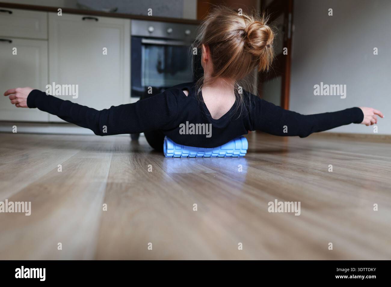 Frau, die sich auf Schaumstoffrolle auf dem Boden der Küche entspannt. Selbstpflege, Rückenentlastung und Stretching-Workout-Konzept. Stockfoto