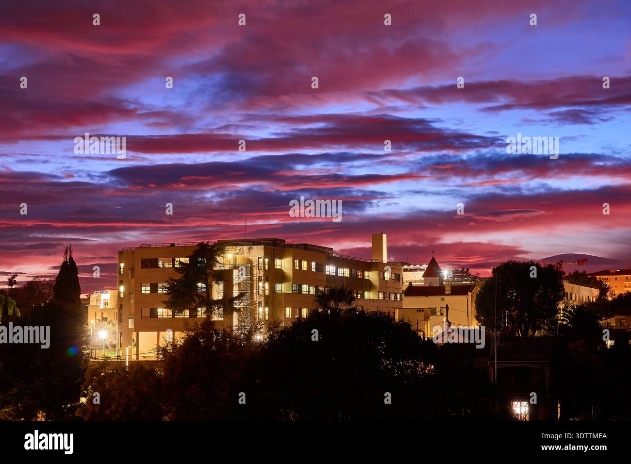 Dramatischer violetter Sonnenuntergang über urbanen Gebäuden mit leuchtenden Fenstern und Skyline von Twilight City Stockfoto