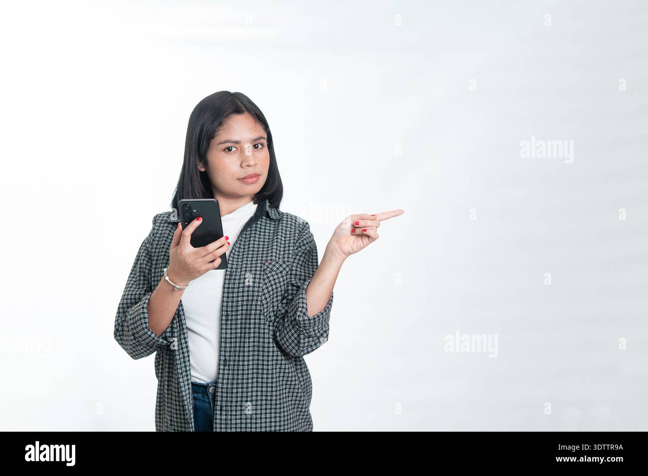 Porträt einer glücklichen indonesischen Frau in einem Flanellhemd, die ein Handy hält und nach oben zeigt. Konzept der digitalen Bildung, Werbung für mobile Apps Stockfoto