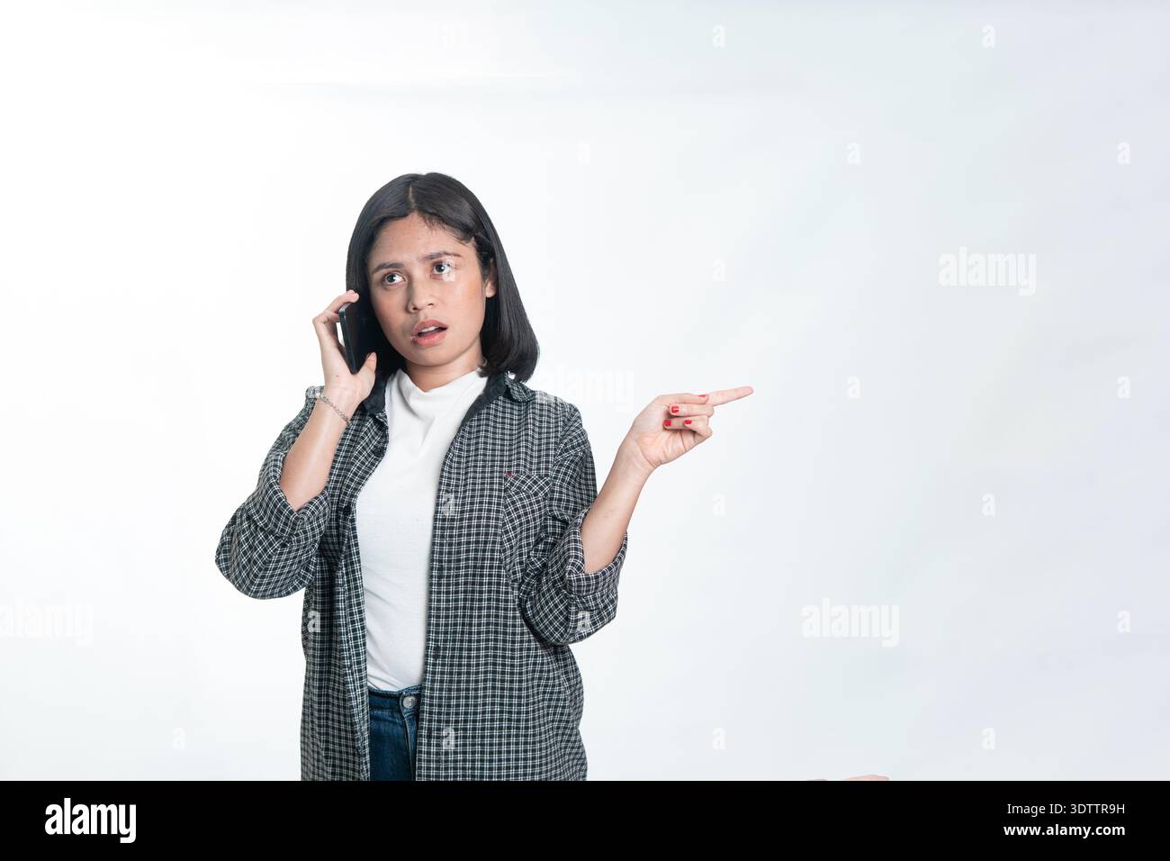 Porträt einer glücklichen indonesischen Frau in einem Flanellhemd, die ein Handy hält und nach oben zeigt. Konzept der digitalen Bildung, Werbung für mobile Apps Stockfoto
