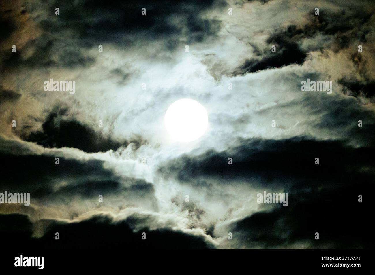 Vollmond mit sichtbaren Kratern in einem dramatischen, bewölkten, schwarzen Nachthimmel. Stockfoto