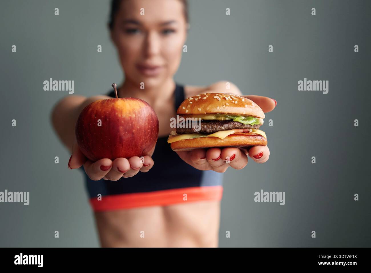 Eine Person hält einen Apfel in der einen Hand und einen Burger in der anderen Hand in einem Fitnessstudio. Stockfoto