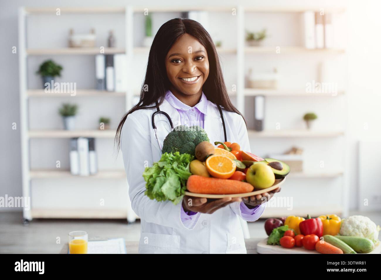 Doctor hält frisches Obst und Gemüse in einer modernen Küchenumgebung für gesunde Ernährung Tipps Stockfoto