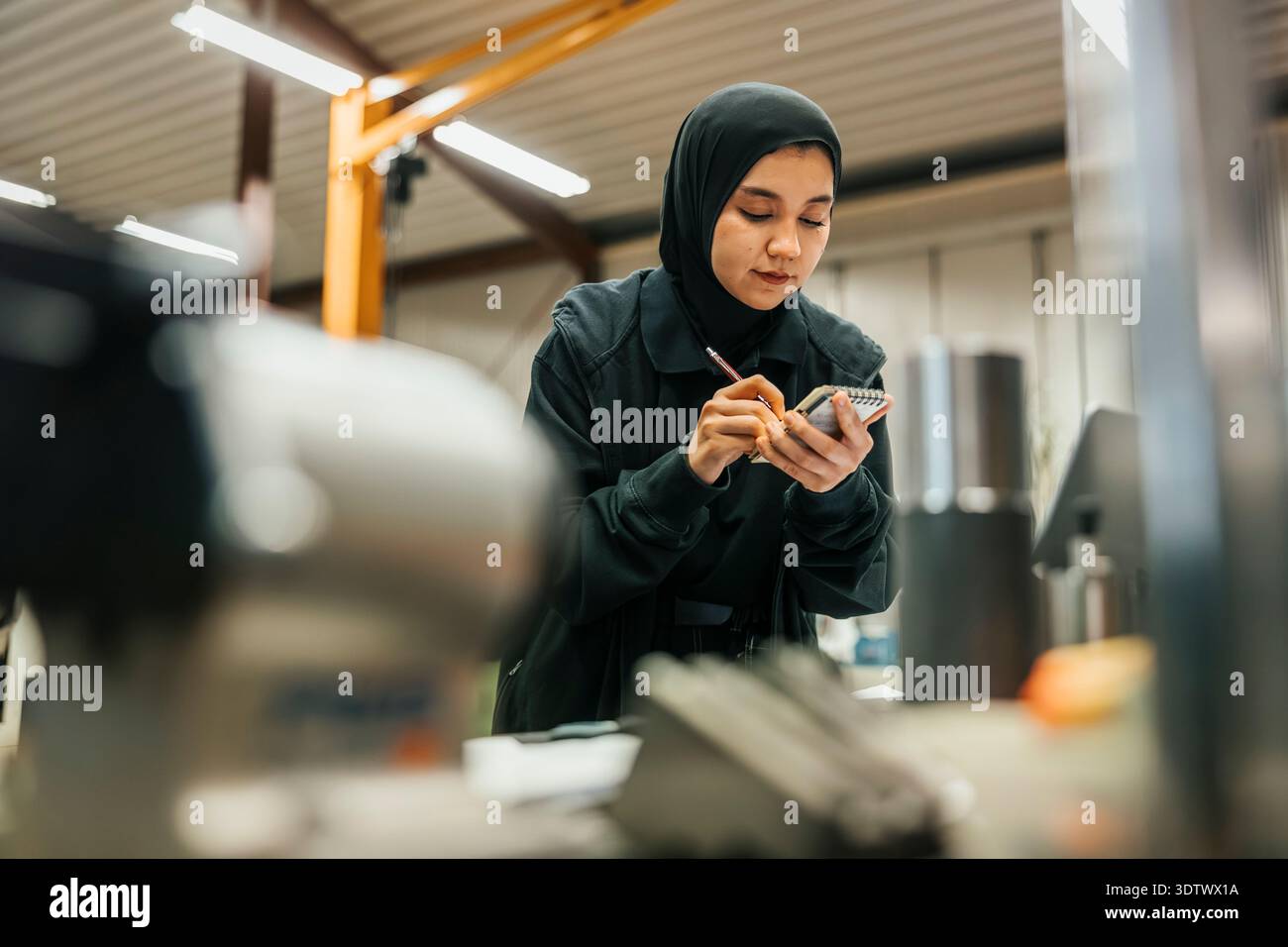 Tiefwinkelansicht einer Fabrikarbeiterin mit Hijab, die Notizen auf dem Notizblock macht Stockfoto