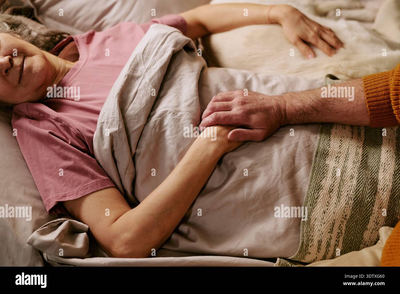Ältere kaukasische Frau, die im Bett liegt und Hände mit einem älteren Mann hält Stockfoto