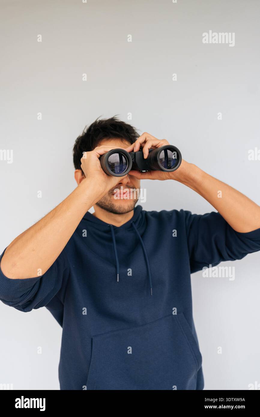 Vertikales Porträt eines neugierigen Mannes, der ein Fernglas an die Augen hält, intensiv nach vorne blickt, aktiv nach neuen Perspektiven sucht, Perspektiven beobachtet und Stockfoto