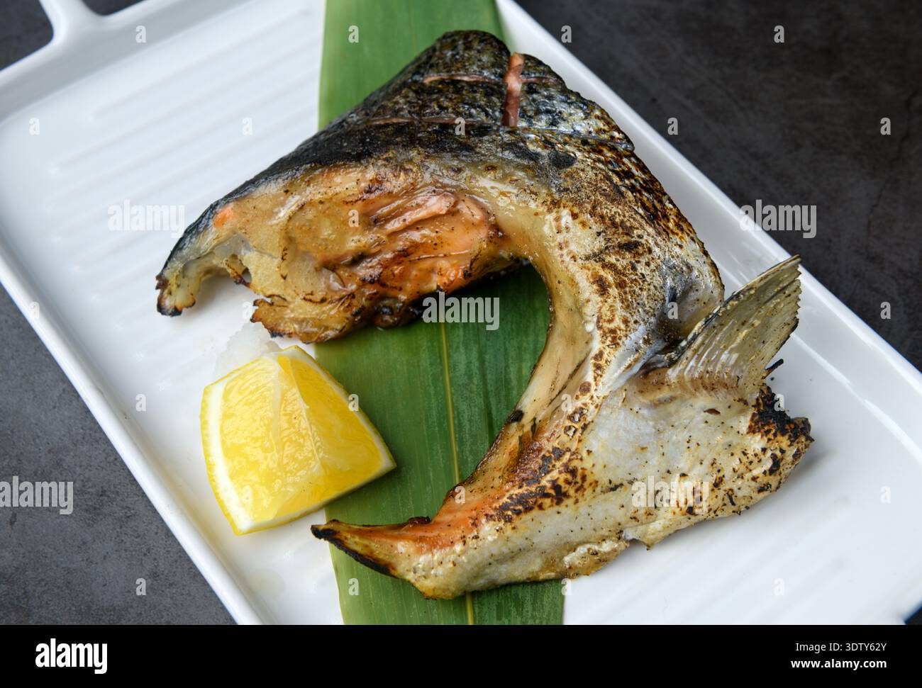 Gegrillter Fischkragen serviert mit Zitrone auf einer weißen Keramikplatte, der einen zarten und geschmackvollen Schnitt präsentiert, der in der japanischen Küche beliebt ist. Stockfoto