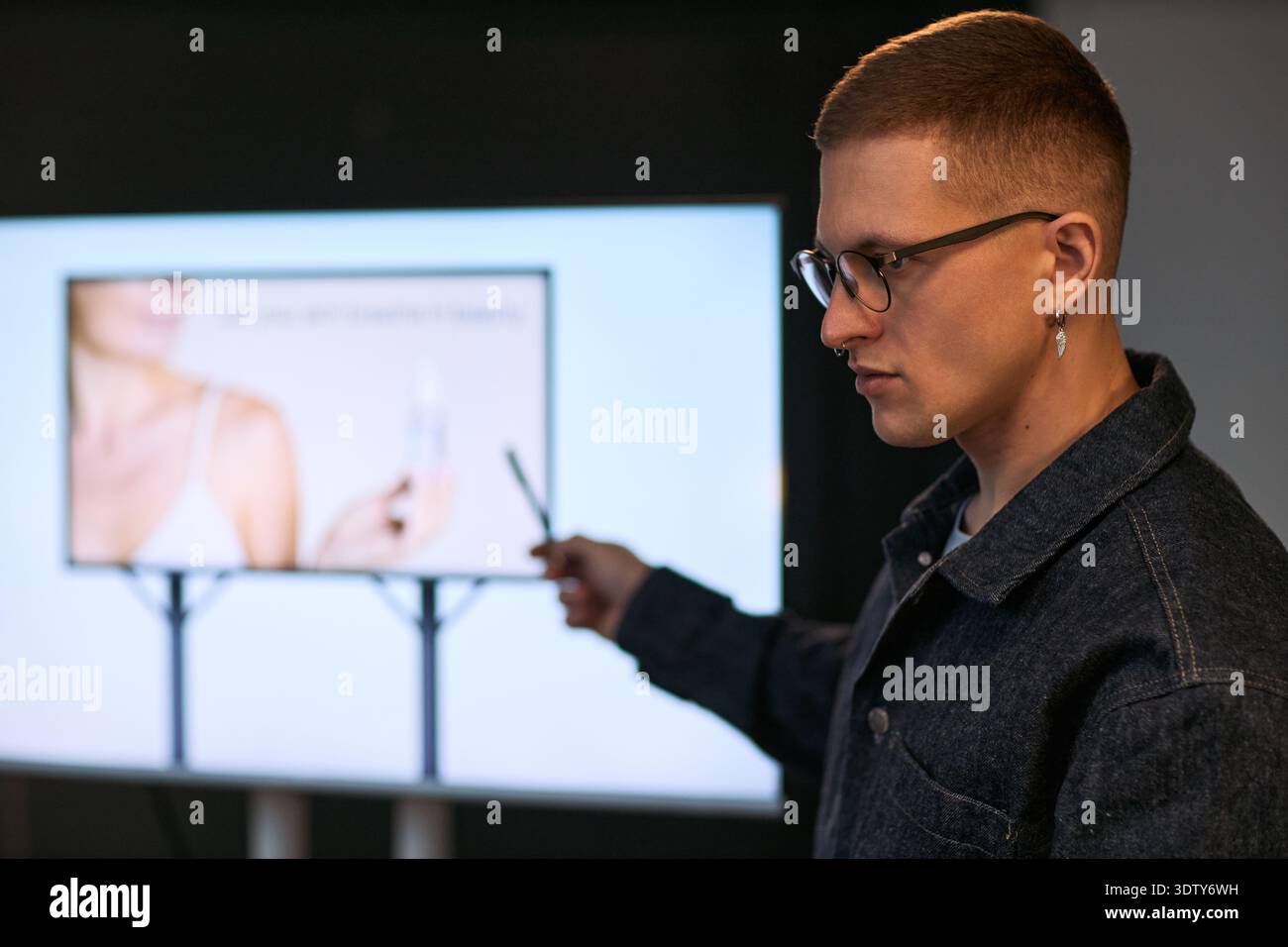 Junger Erwachsener kaukasischer Mann, der Informationen auf dem digitalen Bildschirm präsentiert, Zeiger hält und Gesten auf das Bild einer Frau mit Kosmetikprodukten während der Geschäftspräsentation zeigt Stockfoto