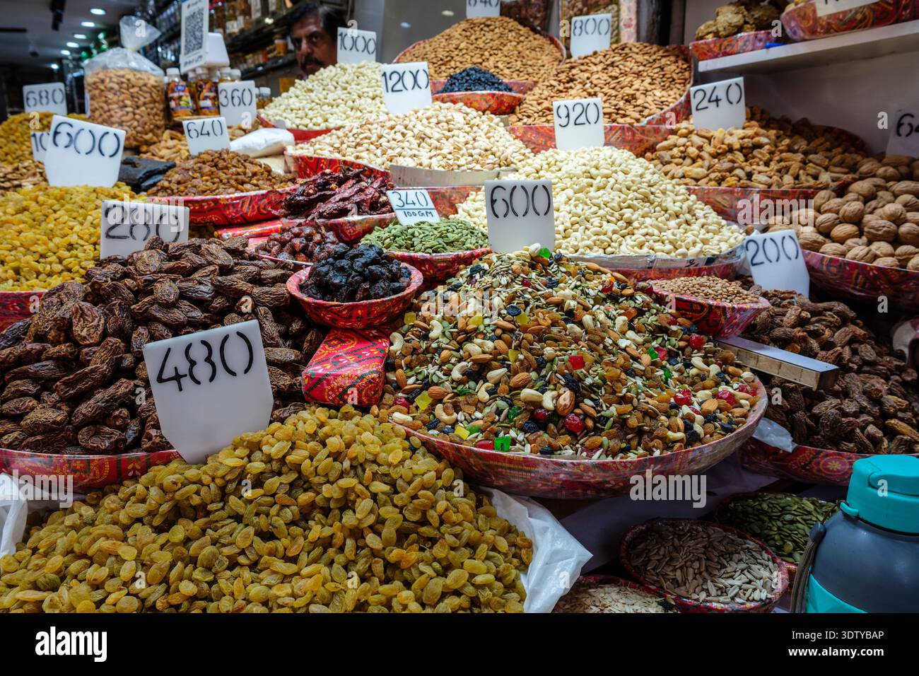 Schüsseln mit Datteln, Rosinen und Nüssen auf dem Gewürzmarkt am Chandni Chowk in Alt-Delhi. Ein Mann ist in der Ferne sichtbar. Stockfoto