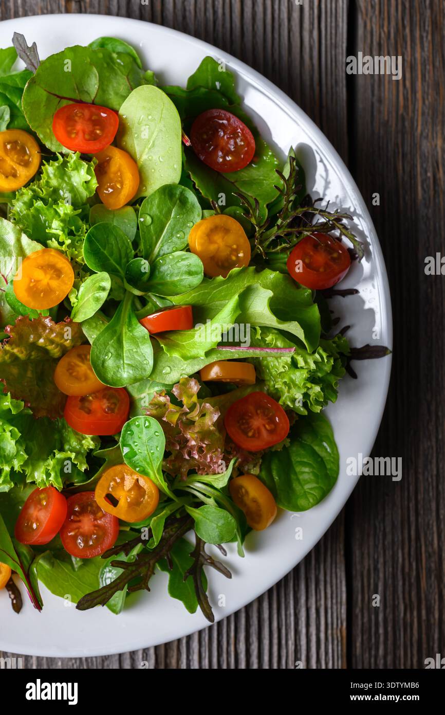 Gemischter Salat mit Kirschtomaten auf weißem Teller. Frisches Blattgemüse auf hölzernem Hintergrund Stockfoto