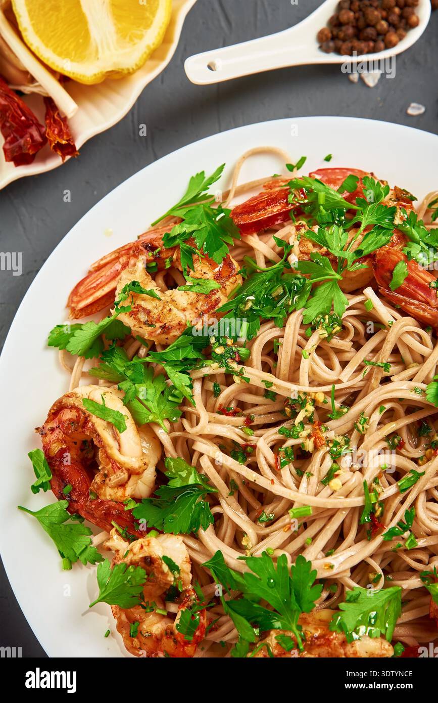 Nudeln mit Garnelen, Zitrone und frischer Petersilie auf weißem Teller unter Rühren braten, Soba mit Garnelen, asiatische Küche, Draufsicht Stockfoto