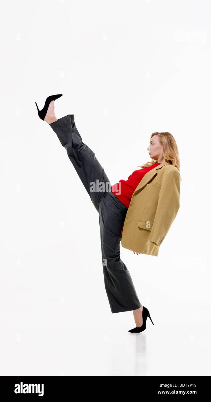 Frau in beigefarbenem Blazer, rotem Pullover und grauer Hose, die hohen tritt auf weißem Hintergrund durchführt. Stockfoto