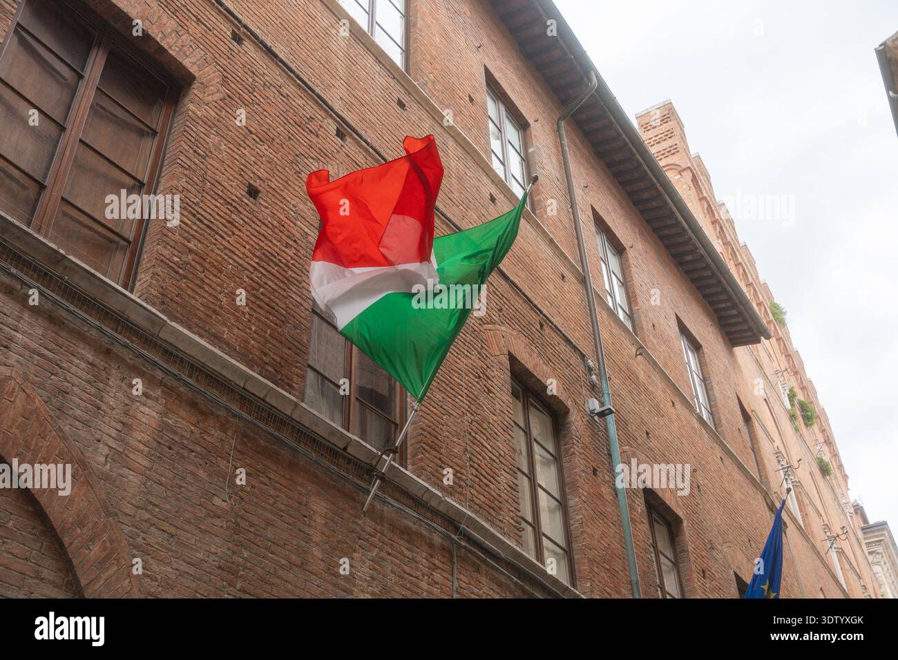 07.06.25, Siena, Italien, Nahaufnahme der italienischen Flagge, die auf der historischen Gebäudefassade winkt. Nationales Symbol und kulturelle Identität Italiens Stockfoto