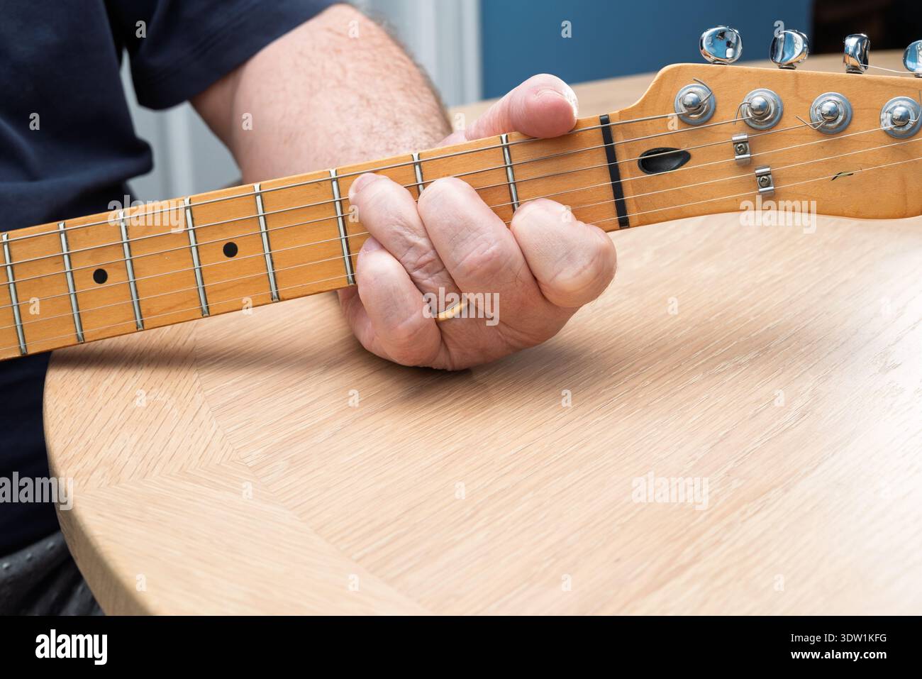 Die Hände einer Person werden beim Spielen einer Gitarre gezeigt, wobei die Finger auf dem Griffbrett positioniert sind, um einen Akkord zu bilden. Stockfoto