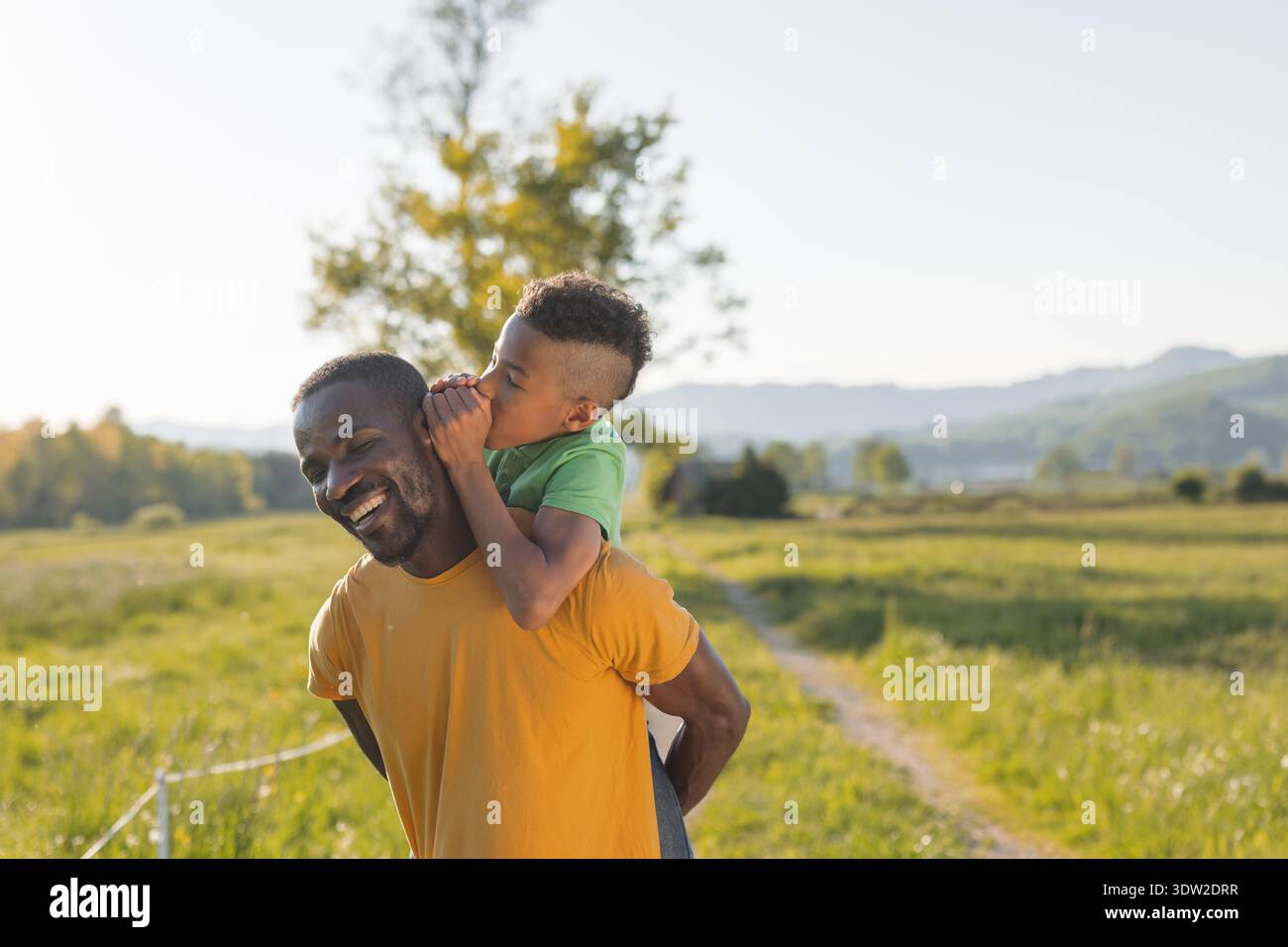Das Flüstern von Vater und Sohn teilt einen glücklichen Moment draußen während des Sonnenuntergangs und genießt spielerische Interaktion in der Natur. Stockfoto