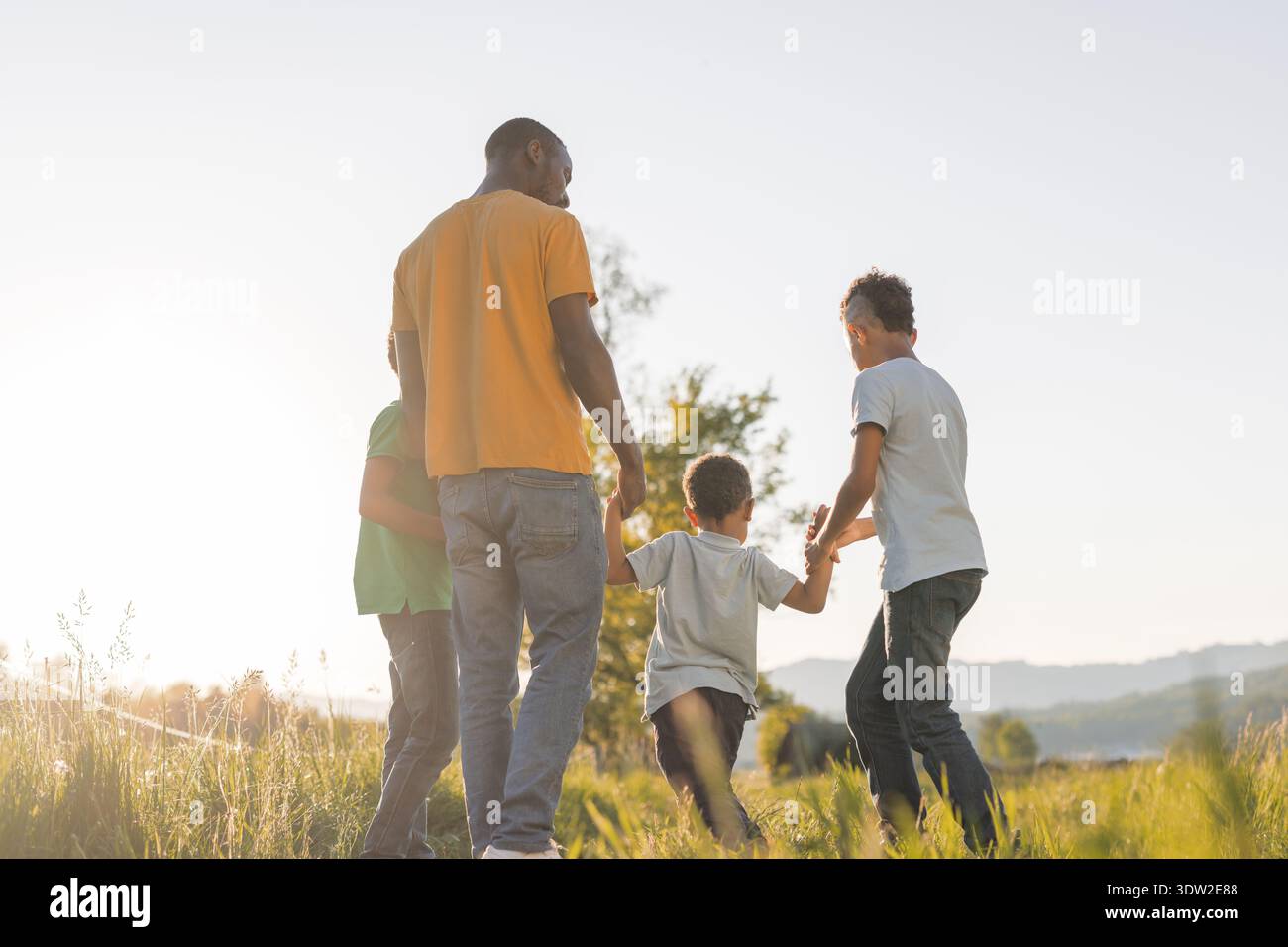Der afroamerikanische Vater spaziert mit seinen Kindern während des Sonnenuntergangs in der Natur, teilt glückliche Momente und verbindet sich als Familie. Stockfoto