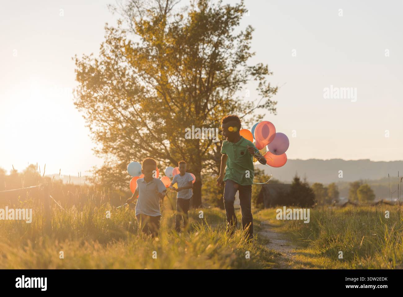 Vater und Kinder laufen während des Sonnenuntergangs durch ein Feld mit bunten Ballons, während sie die gemeinsame Zeit im Freien genießen. Stockfoto