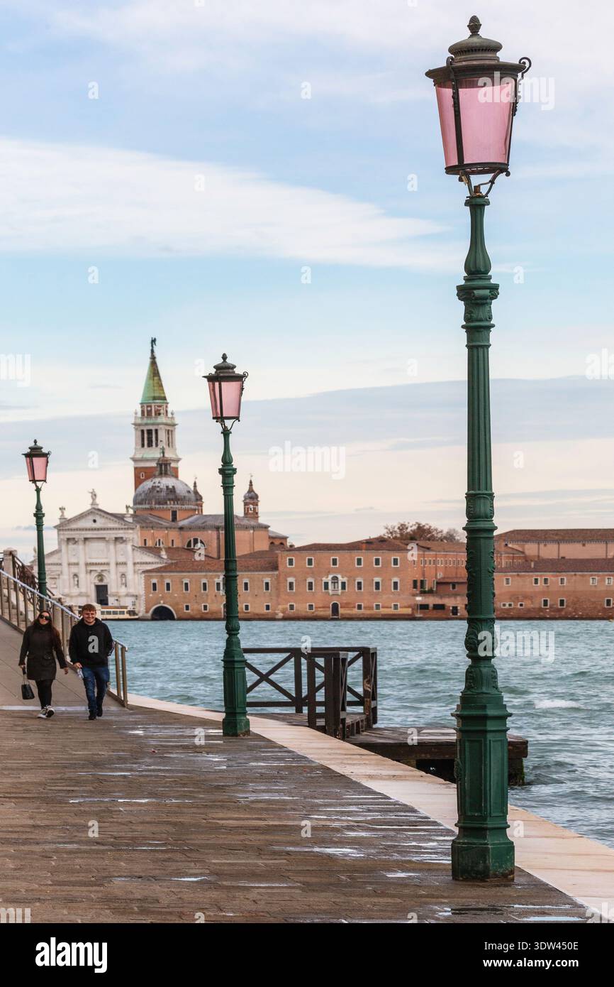 Ein Paar genießt einen ruhigen Spaziergang entlang der malerischen venezianischen Uferpromenade mit historischer Architektur im Hintergrund. Stockfoto