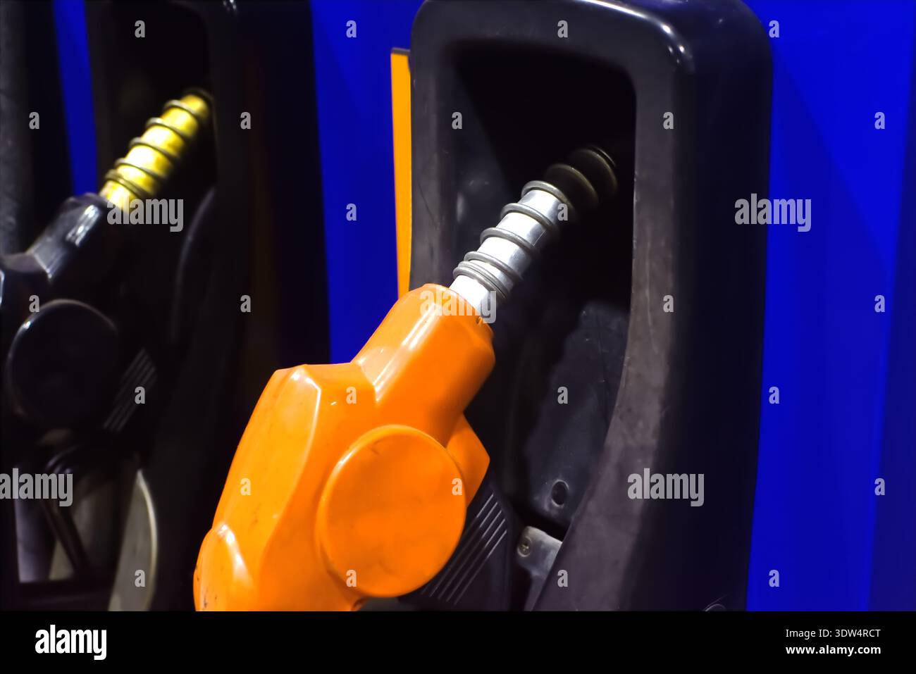 Kraftstoffpumpendüse an einer Tankstelle ist Eine leuchtend orange Kraftstoffpumpendüse in ihrem Holster an einer modernen Tankstelle angedockt. Stockfoto