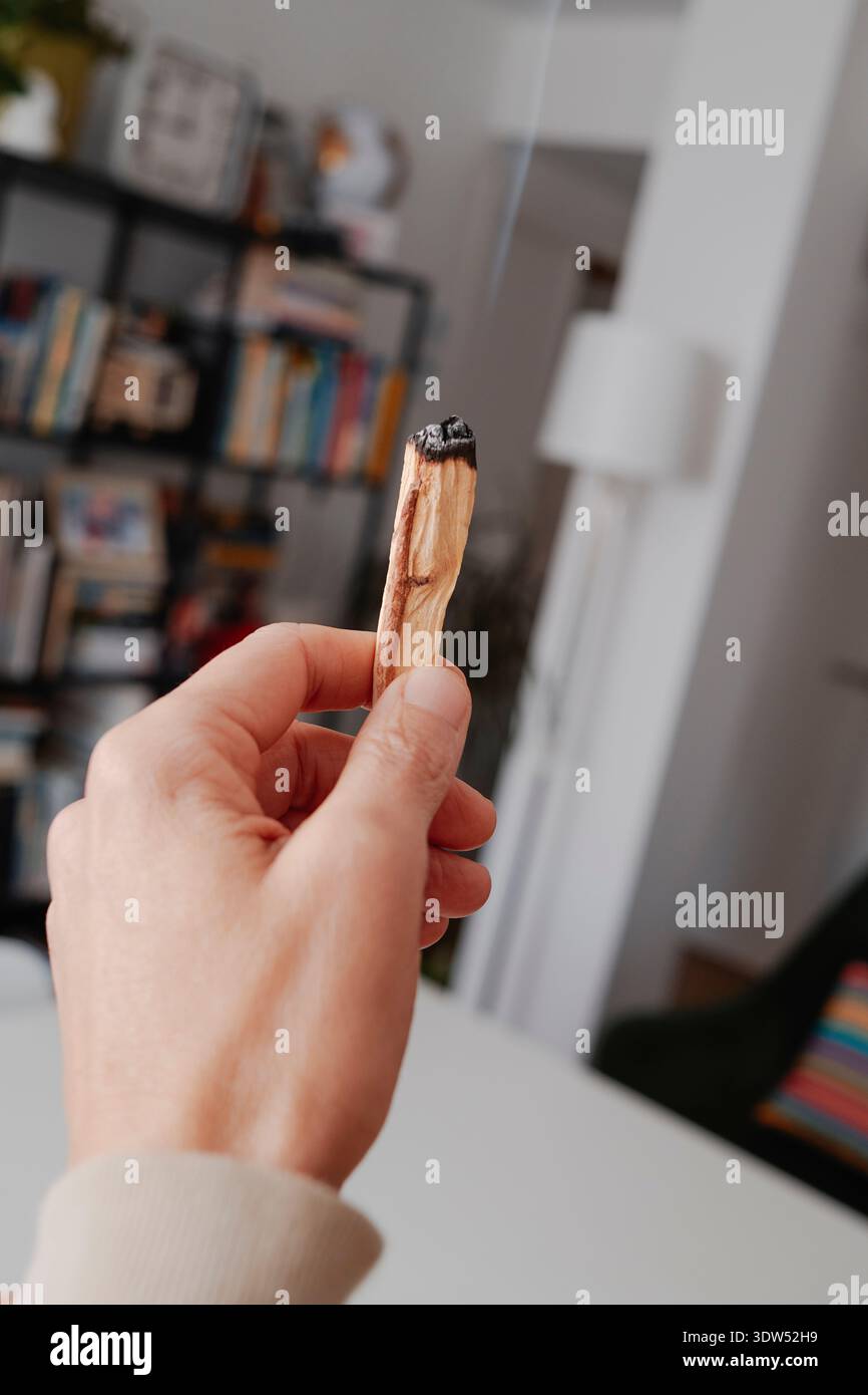In einem Wohnzimmer bewegt ein Mann einen zündeten Sandelholzstab durch die Luft und verbreitet duftenden Rauch, um den Innenraum zu reinigen und zu erfrischen Stockfoto