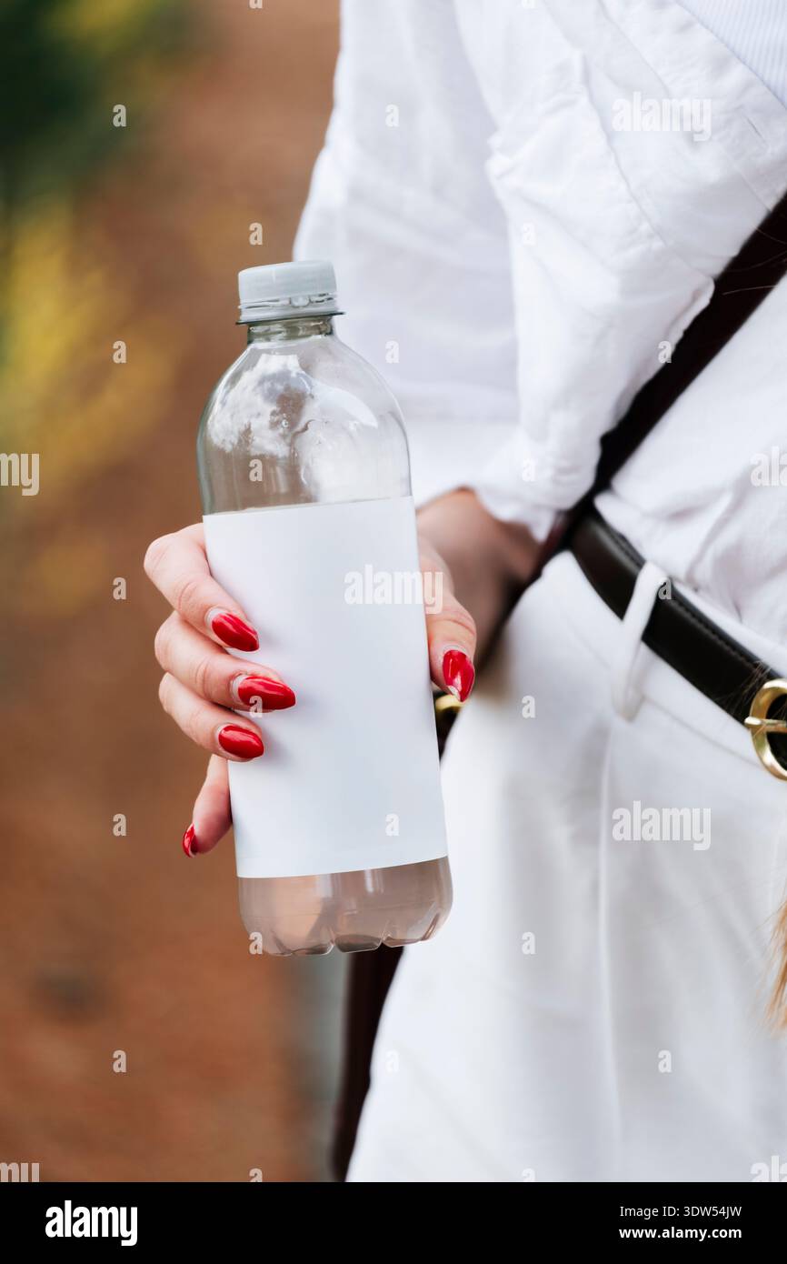 Nahaufnahme einer weiblichen Hand mit einer Kunststoffflasche ohne Branding im Freien mit leerem Etikett, Kopierraum für Branding. Stockfoto