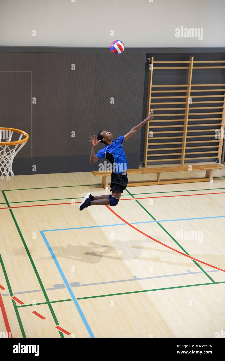 Afroamerikanischer Teenager, der in blauem Trikot rot-weiß-blau-Volleyball auf dem Sportplatz schlägt Stockfoto
