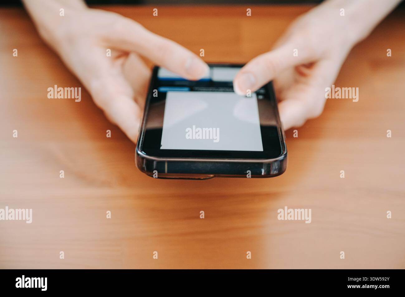 Nahaufnahme von Händen, die ein Smartphone und eine Kreditkarte auf einem Holzschreibtisch halten, als Symbol für Online-Shopping, mobiles Bezahlen und sichere digitale Transaktionen. Stockfoto