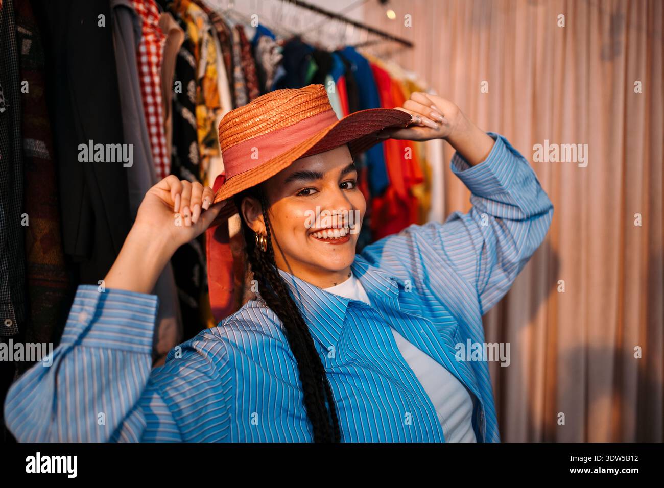 Happy Woman Trial Hat. Frau Trägt Ohrringe Und Gestreiftes Hemd, Die Gerne Einen Hut In Der Boutique Auswählt Stockfoto