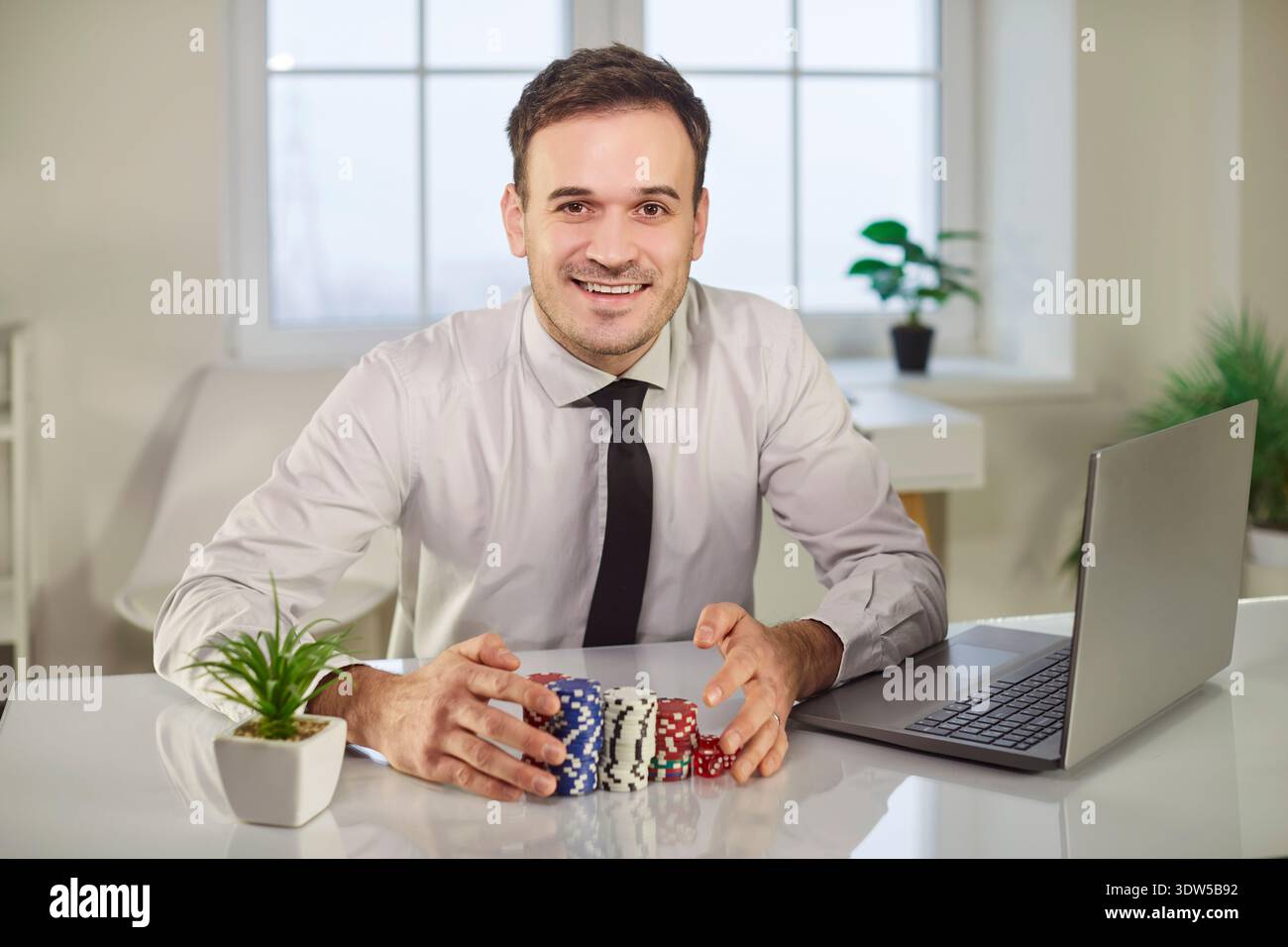 Porträt eines glücklichen lächelnden Mannes, der Poker-Chips hält, der zu Hause sitzt und im Online-Casino gewinnt. Stockfoto