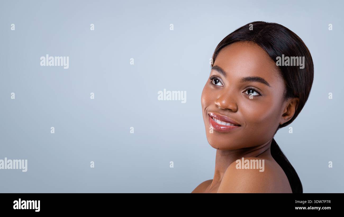 Die schöne Frau lächelt, während sie über ihre Schulter in einem einfachen Studio-Setting schaut Stockfoto