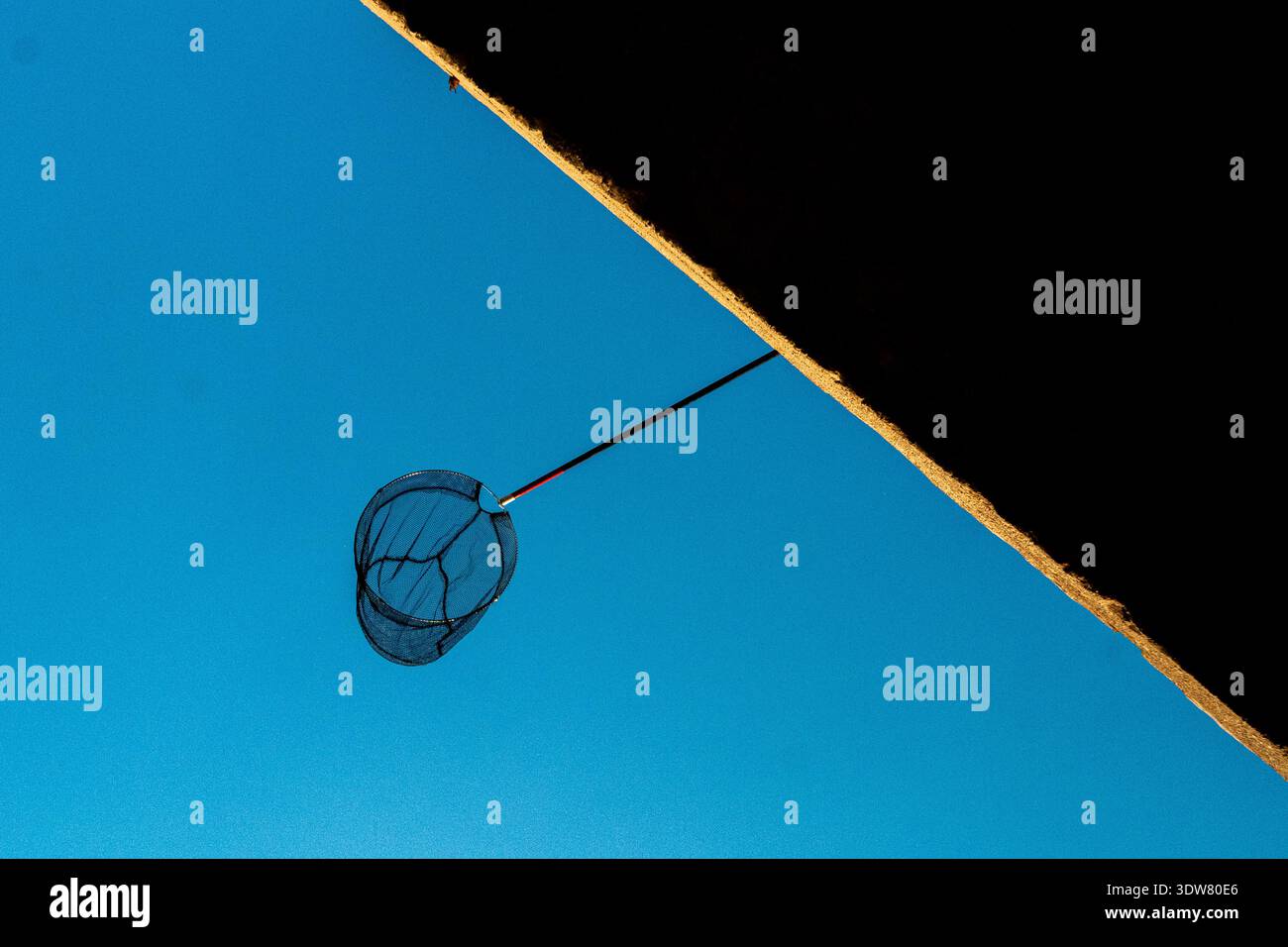 Eine minimalistische Komposition mit einem Fischernetz und einer dunklen diagonalen Wandkante vor einem klaren, hellblauen Himmel. Stockfoto