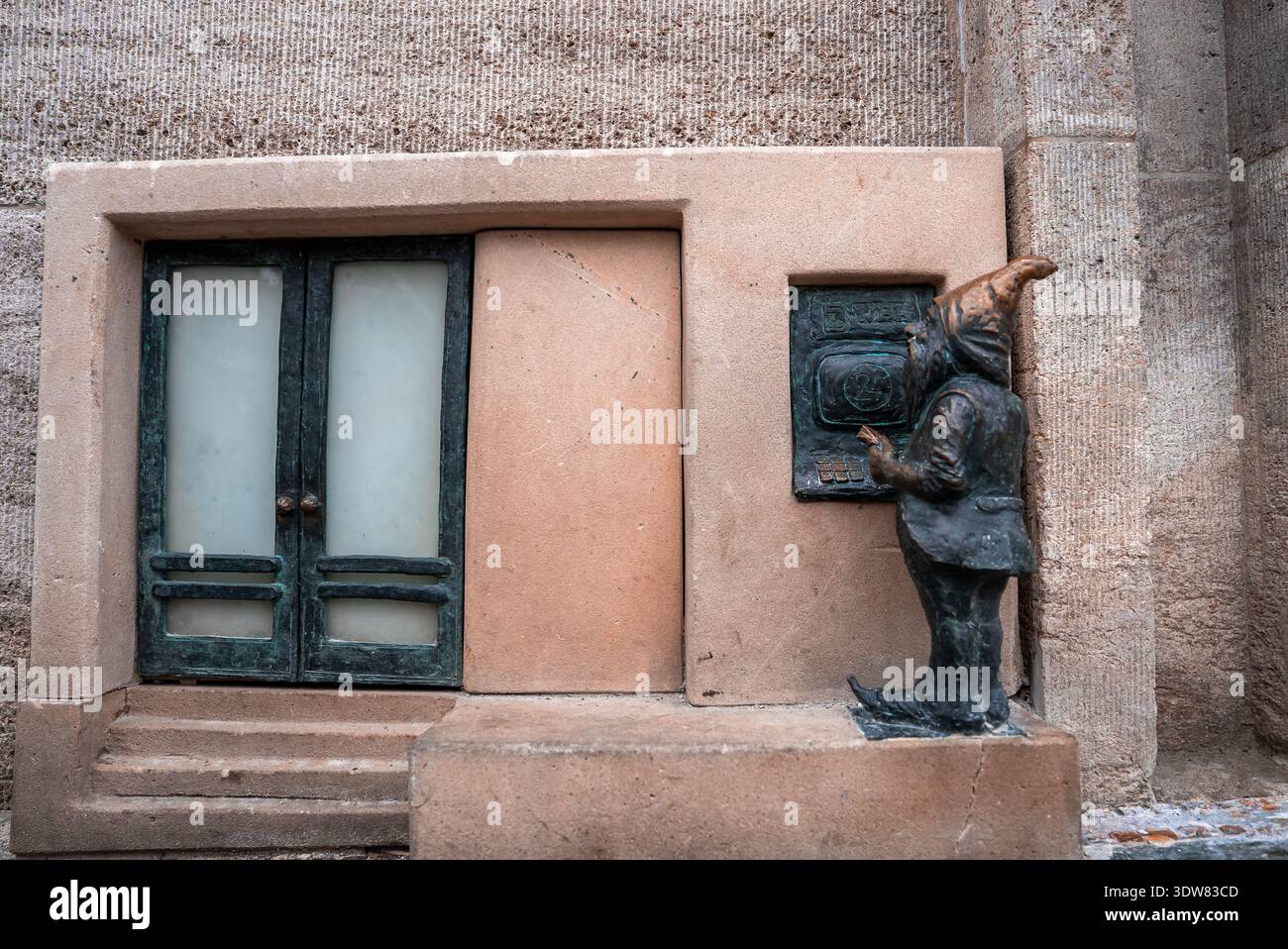 Breslauer Bronzegnoe am Miniatur-Geldautomaten neben winzigen Doppeltüren Stockfoto